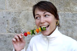 Frau isst fröhlich einen Gemüsespieß